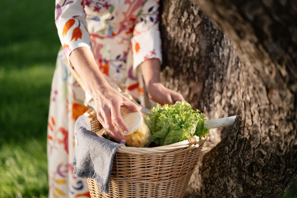 pexels-photo-8417246-8417246 A woman in a floral dress places a jar in a wicker basket outdoors. Fresh produce visible.